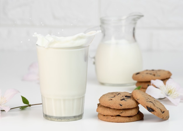 Vaso lleno de leche fresca con salpicaduras se encuentra en una mesa blanca, desayuno saludable