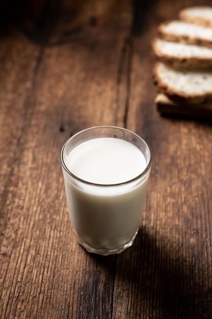 Un vaso lleno de leche El pan en el fondo está borroso Fondo de madera oscura Desayuno matutino Comida saludable Marco vertical