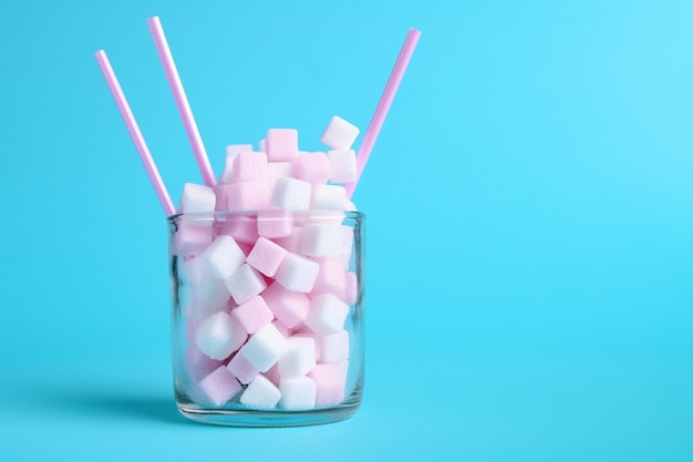 Vaso lleno de terrones de azúcar con paja en rosa pastel