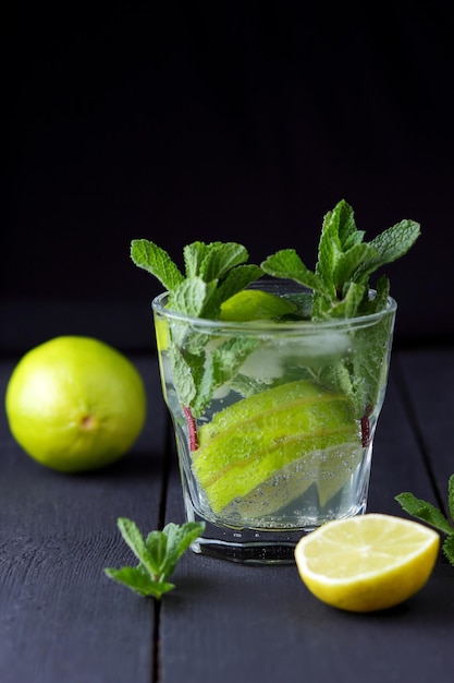 Un vaso de mojito frío con lima limón y menta sobre un fondo de madera negra Primer plano de un refrescante cóctel