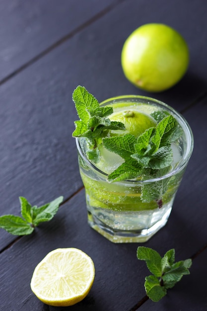 Un vaso de mojito frío con lima limón y menta sobre un fondo de madera negra Primer plano de un refrescante cóctel