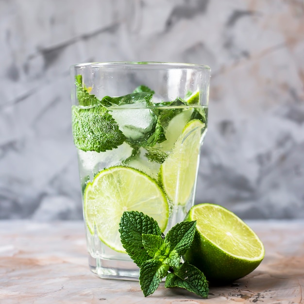 Un vaso de mojito con hielo, menta y limón en un vaso sobre una mesa gris