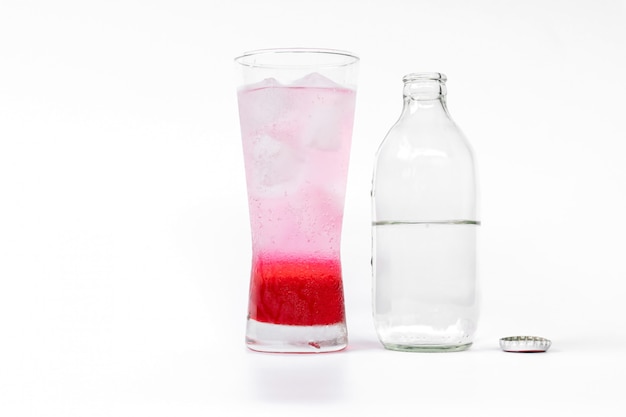 Vaso de néctar rojo mezclado con refrescos y botellas de refrescos que abren la tapa