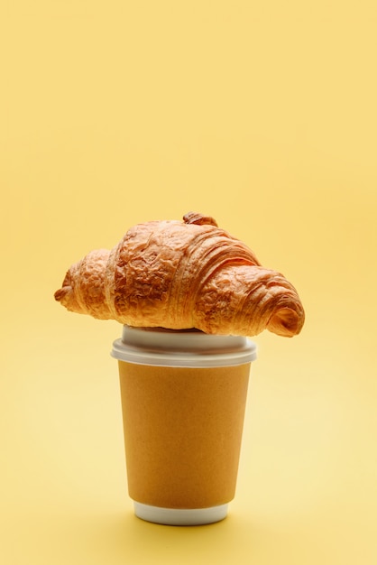 Vaso de papel para café o té con un croissant en la tapa