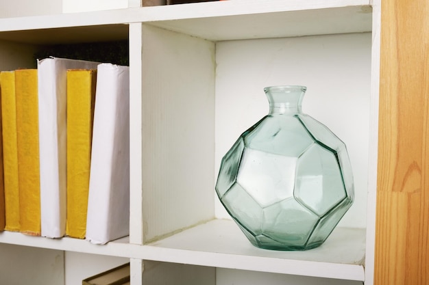 Vaso redondo de vidro verde facetado em uma estante quadrada branca