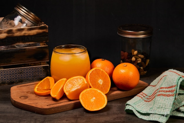 Vaso refrescante con jugo de naranja natural, hielo y naranjas en una mesa de madera en fondo oscuro