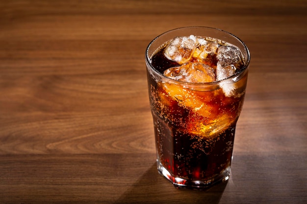 Vaso de refresco de cola con cubitos de hielo en la mesa de madera