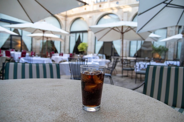 Un vaso de refresco de cola con hielo, burbujas y una rodaja de limón. En la terraza de un restaurante.