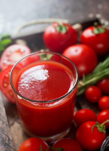 vaso de sabroso jugo de tomate orgánico y tomates frescos y hierbas en bandeja de madera en estilo rústico. Enfoque selectivo, estilo de vida saludable.