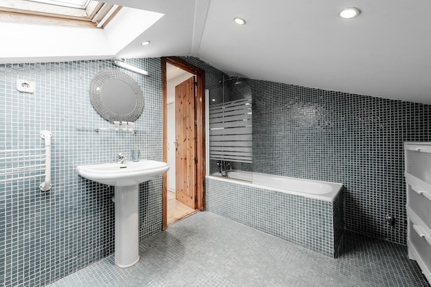 Vaso sanitário grande com teto inclinado revestido com mosaicos nas paredes e piso com sanitários brancos