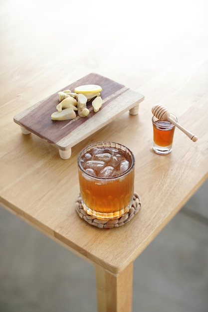 Foto un vaso de sidra de manzana descansa sobre un posavasos de madera junto a una botella de miel y una cuchara de madera.