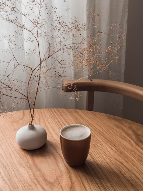 Vaso de taza de capuchino con flores secas en una mesa redonda de madera