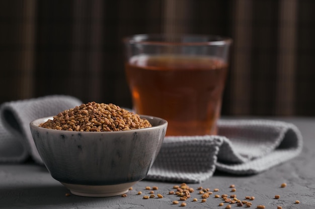 Vaso de té amarillo fenogreco egipcio, bebida Helba o Methi Dana y semillas de fenogreco sobre fondo gris