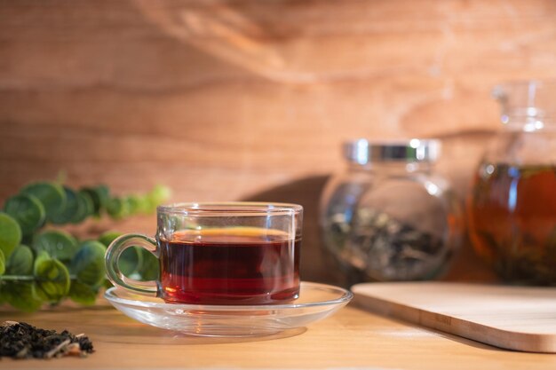 Vaso de té aromático caliente con tetera y hojas de té secas en el fondo