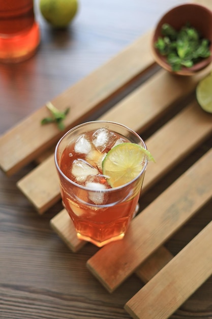 Un vaso de té de bebida fría con cubitos de hielo y lima en una mesa de madera desde arriba