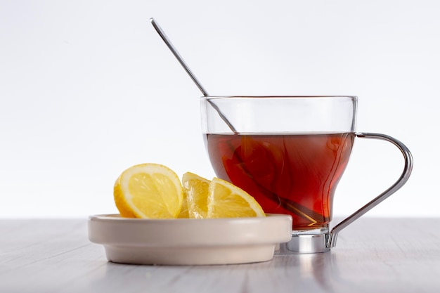 Vaso con té y cucharadita en el interior en una mesa de madera y platillo con rebanadas de limón en un fondo de madera