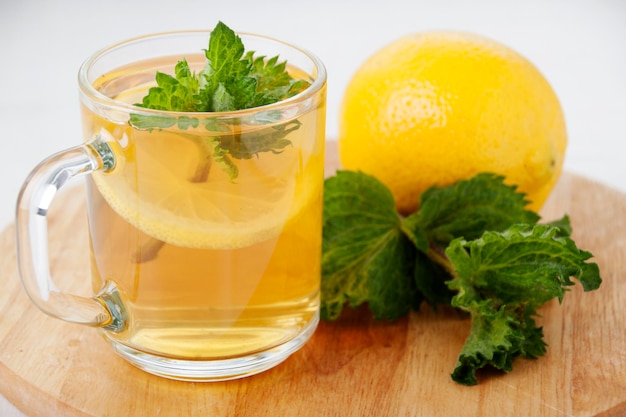 Un vaso de té de limón con un limón y hojas de menta al lado.