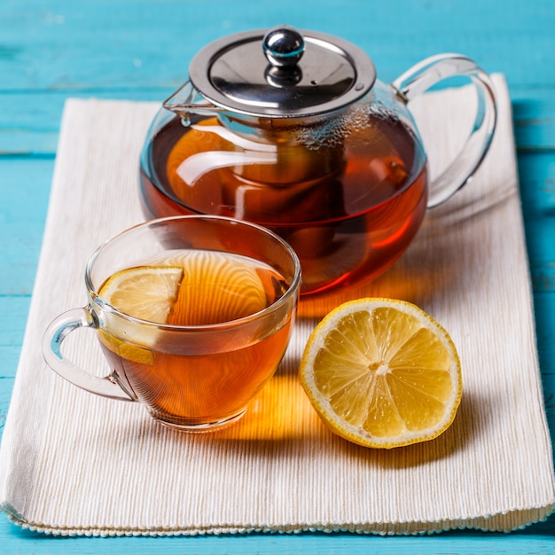 Vaso de té con limón y tetera de vidrio.