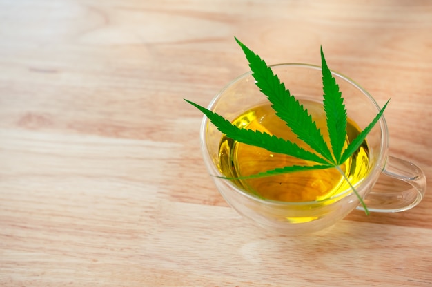 Un vaso de té de marihuana caliente sobre la mesa de madera. Té de hierbas de cannabis con hoja verde.