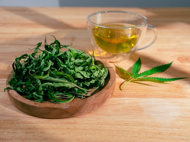 Un vaso de té de marihuana caliente sobre la mesa de madera. Té de hierbas de cannabis con hojas secas.