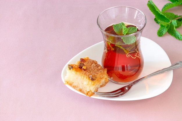 Vaso de té de menta marroquí con Basbousa (namoora) tradicional tarta de sémola árabe con nuez de almendra y almíbar. Copie el espacio. Enfoque selectivo. Fondo rosa.