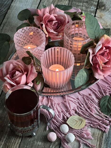 Un vaso de té en un portavasos candelabros de cristal rosa con velas y rosas en una tarjeta de mesa de madera