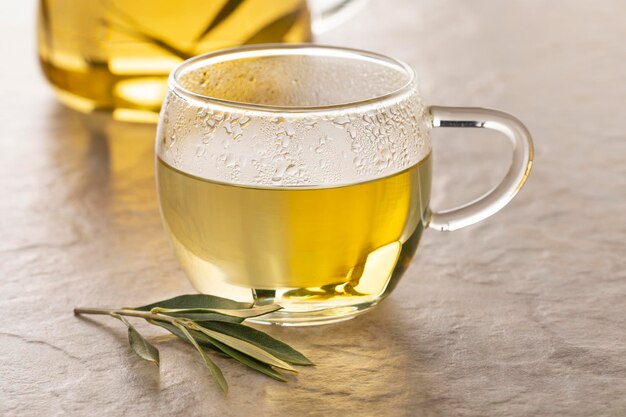 Vaso de té con té de hojas de olivo secas y una ramita fresca de hojas de olivo delante