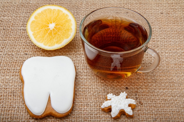 Vaso de té, trozo de limón y galletas de jengibre en forma de estrella y diente en la mesa con cilicio.