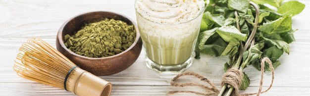 Foto un vaso de té verde matcha con crema batida en una mesa blanca con menta en polvo y batido