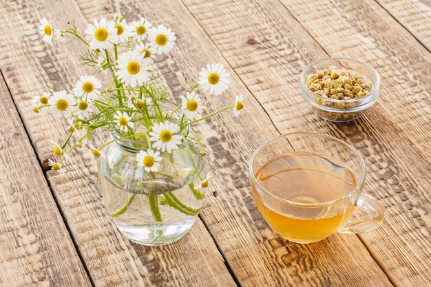 Vaso de té verde, tarro con flores de manzanilla blancas y flores secas de matricaria chamomilla