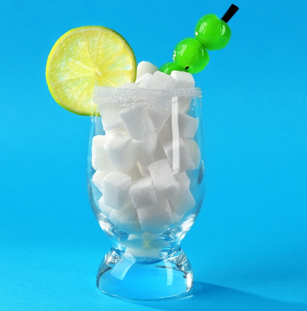 Vaso con terrón de azúcar cóctel cerezas y rodaja de limón sobre fondo azul.