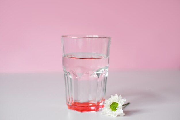 Un vaso transparente con agua potable se encuentra sobre un fondo rosado