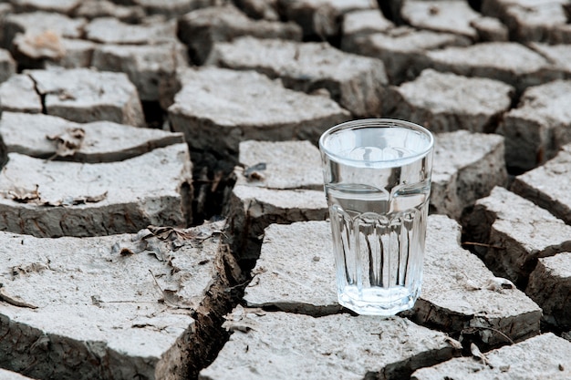 Un vaso transparente de agua potable limpia se encuentra en medio de una tierra desértica seca y agrietada. Concepto de calentamiento global. Sequía y crisis del agua