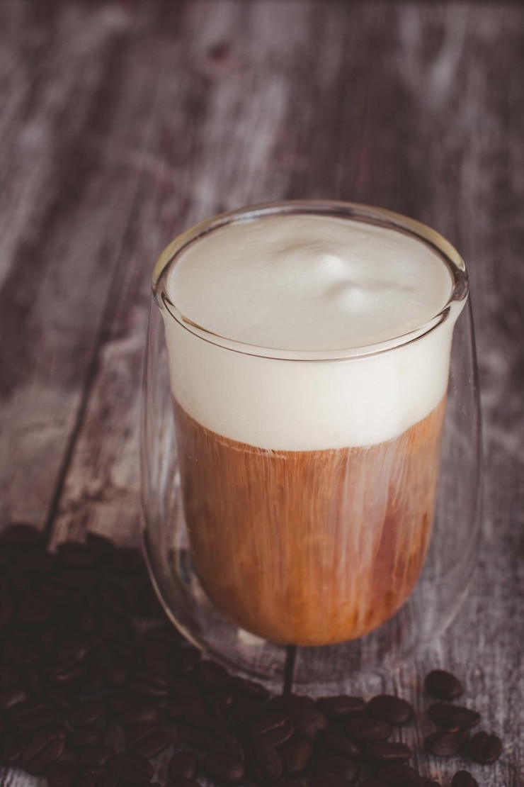 Foto vaso transparente de café con espuma de leche y grano de café tostado sobre un fondo de madera