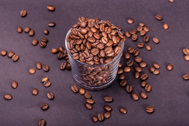 Vaso de vidrio con granos de café naturales tirados en el suelo sobre un fondo negro continuo Día Internacional del Café 1 de octubre