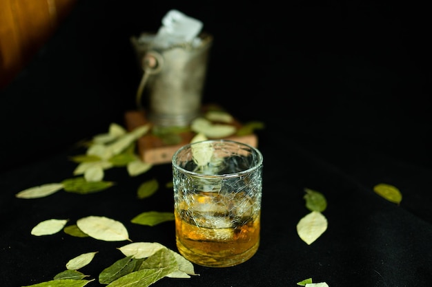 Vaso de vidrio con licor y hojas secas sobre una mesa negra