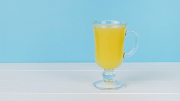 Un vaso de vidrio en una pierna sobre una mesa de madera blanca sobre un fondo azul.