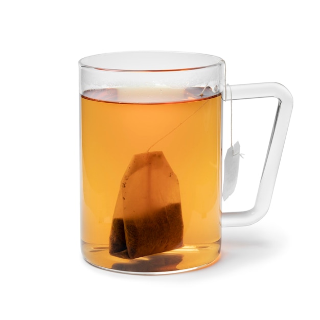 Vaso de vidrio con té y una bolsita de té sobre fondo blanco.