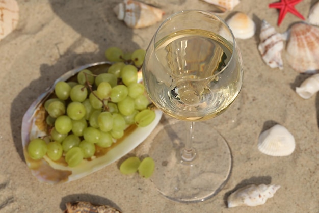 vaso de vino blanco sobre la arena como fondo con conchas