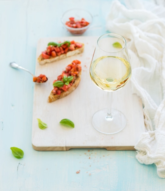 Vaso de vino blanco, tomate y albahaca bruschetta sandwich en tablero de madera pintada