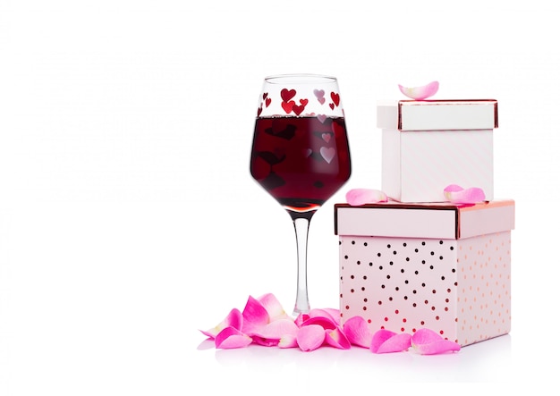 Vaso de vino tinto con corazón y caja de regalo rosa y rosa para el día de san valentín sobre fondo blanco.