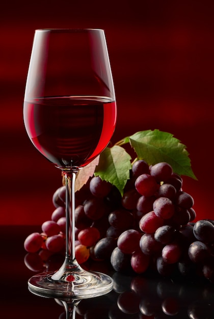 Un vaso de vino tinto y uvas sobre una mesa brillante.