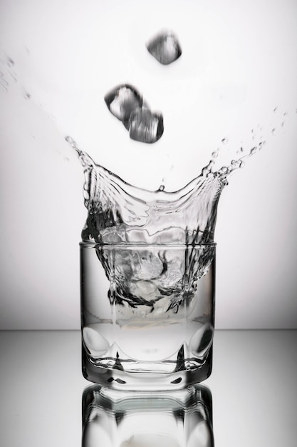 Vaso con vodka, alcohol, agua sobre un fondo gris con trozos de hielo cayendo sobre él con salpicaduras