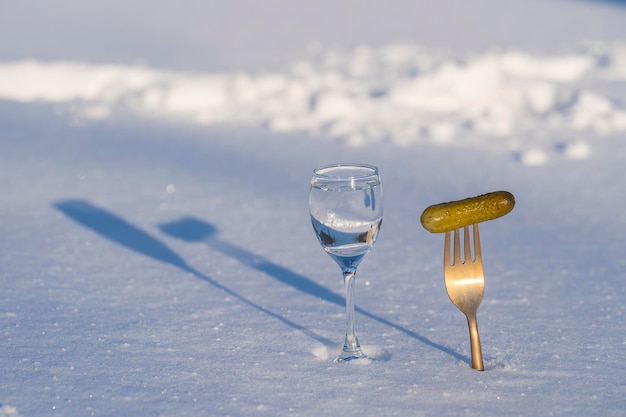 Vaso de vodka y un tenedor con pepino en vinagre sobre una nieve blanca en invierno de cerca