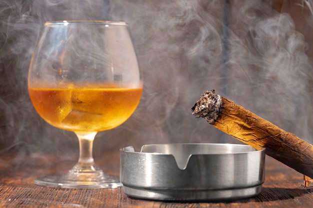 Vaso de whisky y cigarro encendido en un cenicero