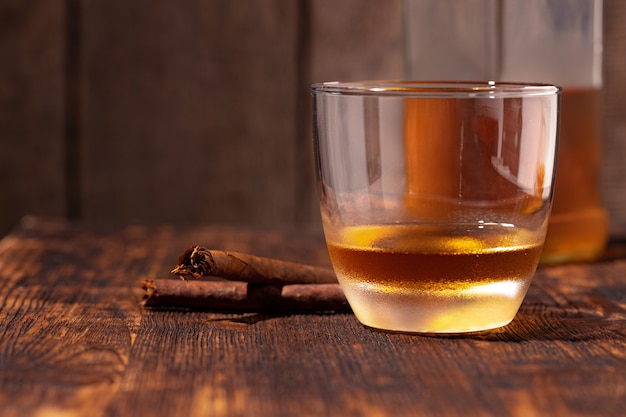 Un vaso de whisky y cigarro en la mesa de madera de cerca