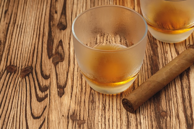 Vaso de whisky y cigarros enrollados sobre mesa de madera
