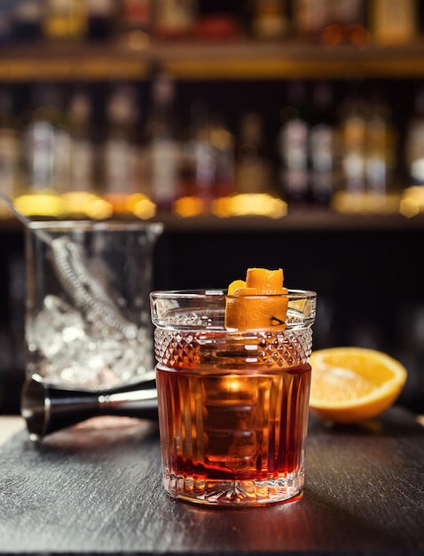 Vaso de whisky coñac o brandy con limón y cubitos de hielo de pie en el mostrador del bar con una botella en el fondo