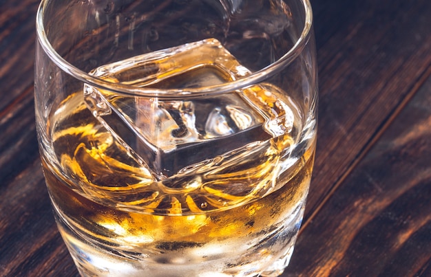 Vaso de whisky con cubitos de hielo en la mesa de madera