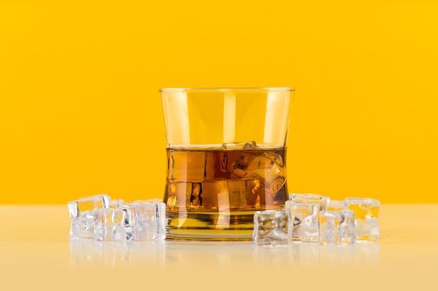 Vaso de whisky con cubitos de hielo sobre fondo amarillo